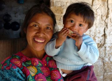 Indigene Frau mit kleinem Kind auf dem Arm, der etwas isst.