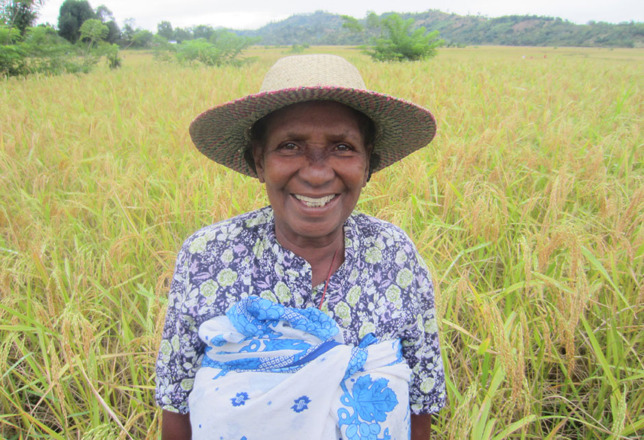 Frau in Madagaskar unseres Projektes "Fluss des Lebens" steht in einem grünen Feld