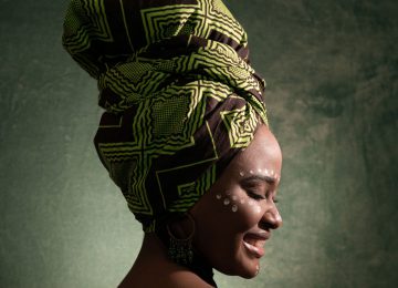 Afrikanische Frau im seitlichen Profl mit buntem Turban lächelt.