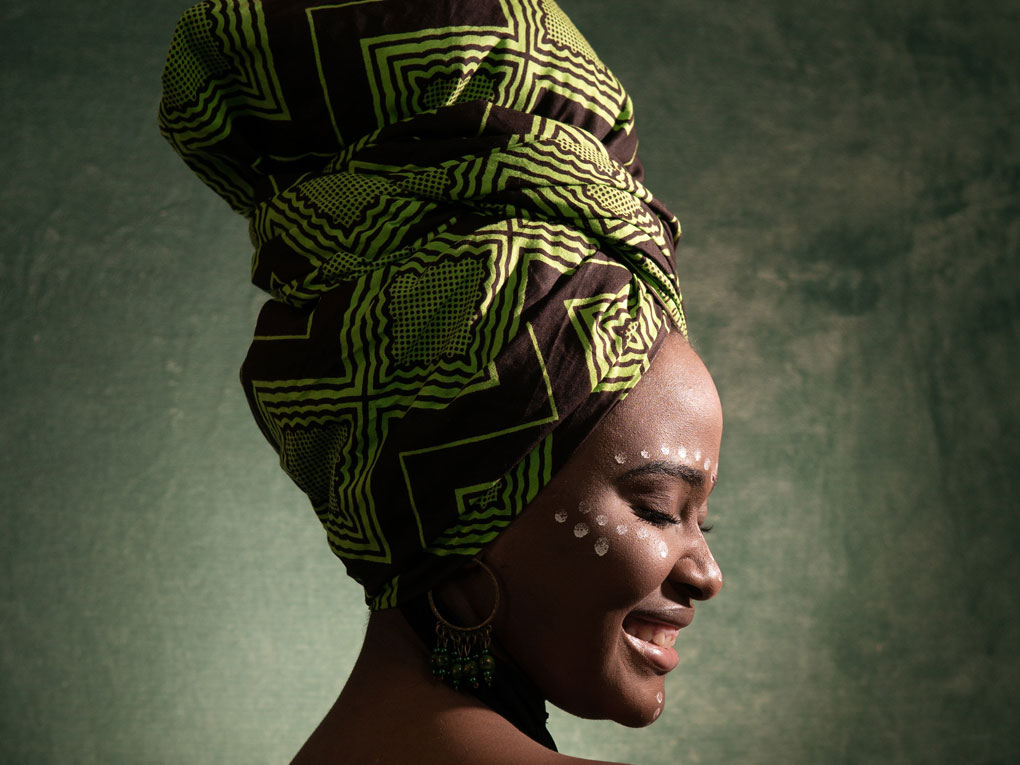 Afrikanische Frau im seitlichen Profl mit buntem Turban lächelt.