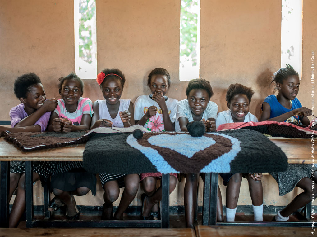 Mädchen in Sambia sitzen auf einem Tisch und lachen, vor Ihnen ein gewebtes Herz