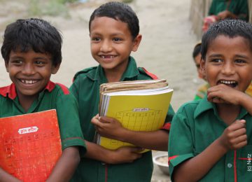 3 kleine Buben aus Bangladesch haben Schulbücher in der Hand und freuen sich, dass sie Grundschulbildung erhalten