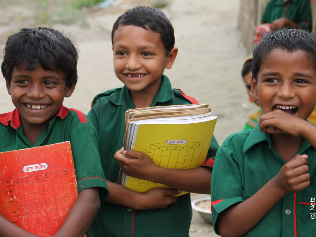 3 kleine Buben aus Bangladesch haben Schulbücher in der Hand und freuen sich, dass sie Grundschulbildung erhalten