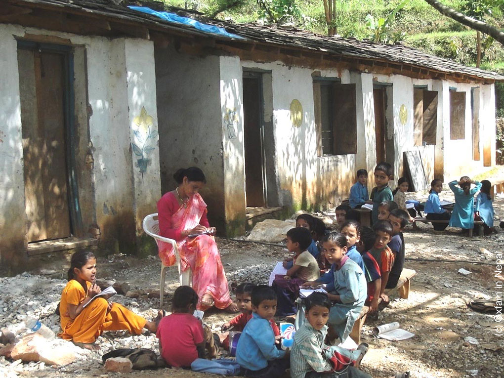 Kinder in Nepal sitzen am Boden unter einem Baum und um ihre Lehrerin herum. Sie freuen sich, dass sie Schulbildung erhalten.