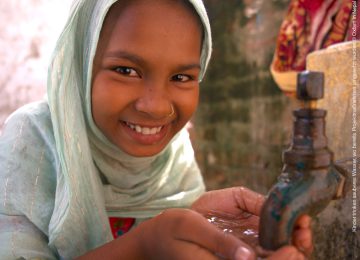 Mädchen aus Nepal hält die Hände unter einen laufenden Wasserhahn und freut sich