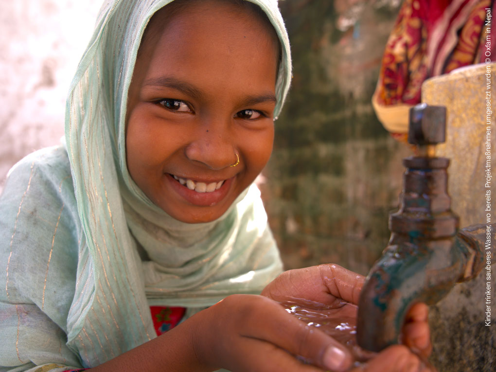 Mädchen aus Nepal hält die Hände unter einen laufenden Wasserhahn und freut sich