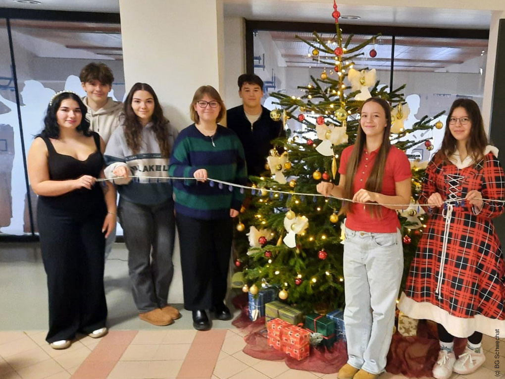 SchülerInnen des BG Schwechats stehen vor einem geschmückten Weihnachtsbaum und freuen sich über eine erfolgreiche Spendenaktion für den Entwicklungshilfeklub.