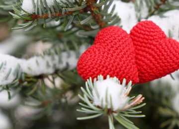 zwei stoffherzen im Schnee auf einem tannenzweig.