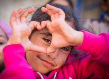 Ein geflüchtetes Mädchen aus Syrien formt ein Herz mit ihren Händen.