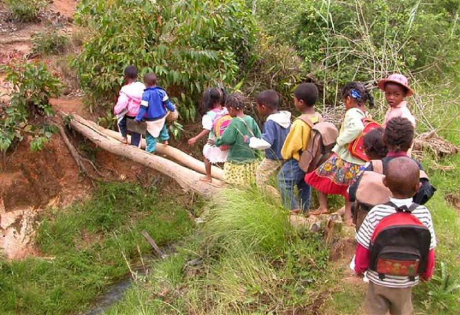 Kinder überqueren zur Schule den Fluss über Baumstämme