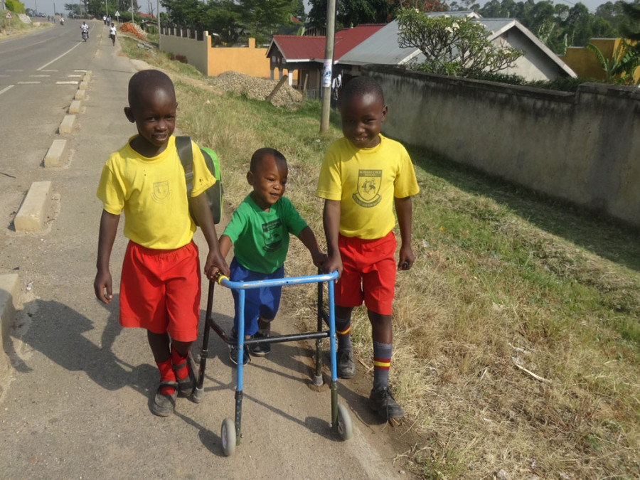 Drei Kinder von denen eines sich mit Hilfe einer Gehhilfe vorwärts bewegt