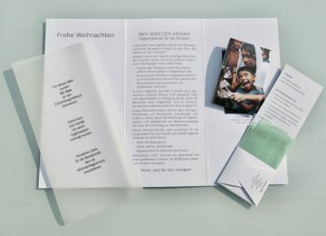 Weihnachts-Anstatt-Billet im aufgeklapptem Zustand mit Transparentpapier und Seifenpäckchen.