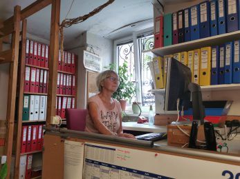Frau vorm Computer sitzend mit Ordner im Hintergrund