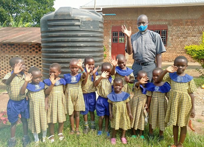 Fr. Joseph Kasangaki und seine Kindergartenkinder vor ihrem neuen Wassertank in Uganda