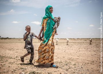 Frau mit 2 Kindern, die über dürren Boden gehen.