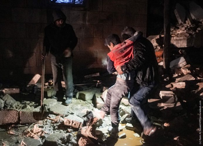 Erdbeben in Syrien und Türkei, eine Mann stützt verwundeten Jugendlichen in einem zerstörten Gebäude