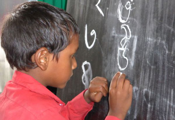 Für alle Mädchen und Buben der Vor- und Grundschule werden Lehr- und Lernmaterialien wie Tafeln, Kreide, Schulbücher, Hefte, Stifte … angeschafft, damit auch wirklich alle die gleiche Chance bekommen. Ein Bub schreibt an eine Tafel