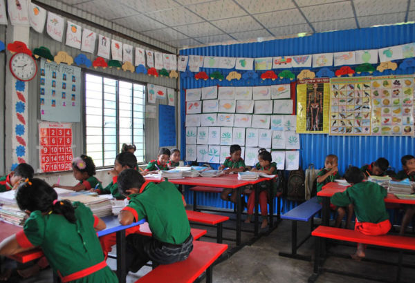 Die Sitzordnung im Klassenraum ist nicht frontal, sondern in Gruppentischen. Die Wände sind mit Lernpostern und Bastelarbeiten geschmückt. Die Klassen-größen von 30 Kindern ermöglichen es, gezielt auf individuelle Bedürfnisse einzugehen. Kinder sitzen im Klassenraum an Gruppentischen