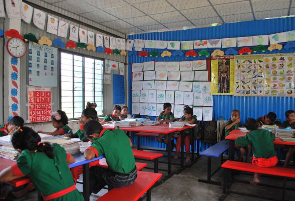 Die Sitzordnung im Klassenraum ist nicht frontal, sondern in Gruppentischen. Die Wände sind mit Lernpostern und Bastelarbeiten geschmückt. Die Klassen-größen von 30 Kindern ermöglichen es, gezielt auf individuelle Bedürfnisse einzugehen. Kinder sitzen im Klassenraum an Gruppentischen