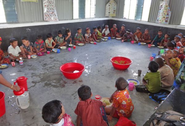 In der jährlichen Hungerperiode zwischen den Erntezeiten bekommen alle Schülerinnen und Schüler warme Schulmahlzeiten. Das fördert ihre Konzentration und sichert ihre Teilnahme am Unterricht. Schülerinnen und Schüler sitzen auf dem Boden und essen