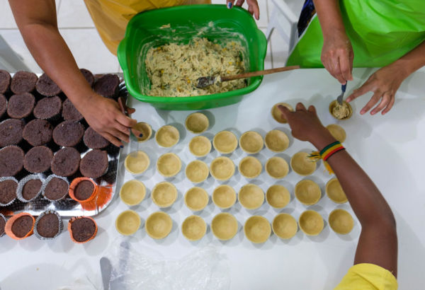 In den praktischen Kurseinheiten lernen die Teilnehmerinnen die Herstellung verschiedener Süßspeisen wie Kuchen, Torten oder Pudding sowie pikanter Backwaren wie zum Beispiel mit Fleisch, Käse oder Fisch gefüllter Teigtaschen. Mehrere Hände über einem Tisch mit Backwaren