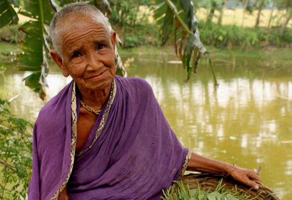 Die 70 Jahre alte Manoda verkauft unter anderem Betelblätter in den Dörfern. Sie hat mittlerweile eine Kuh, Schafe, einen Gemüsegarten. Sie hat drei Mal am Tag zu essen. Es geht ihr wieder gut. Alte Frau am Fluss mit Korb voll Blättern