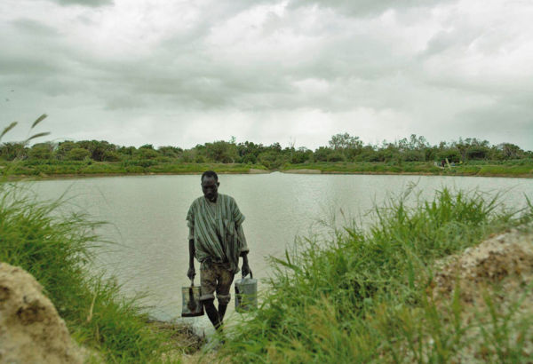 Wenn der Bouli gefüllt ist und die Gemüsegärten angelegt sind, wird das Wasser für die Saat und die Pflanzen mit Gießkannen herbeigeholt. Mann holt Wasser mit Gießkannen vom Wasserreservoir