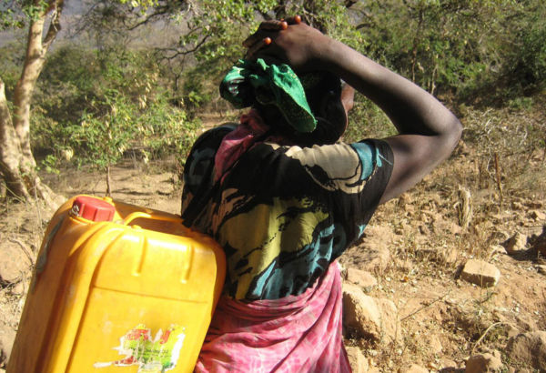 Die Sicherung der Wasserversorgung erleichtert den Hirtenfamilien ihr Leben in vielen Bereichen. Da sich der Wassertank im Dorf befindet, müssen die Mädchen fürs Wasserholen nicht mehr mehrere Kilometer weit gehen. Frau trägt Wasserkanister am Rücken